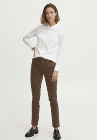 Bielo košeľu s golierom, skombinovanú s hnedými slim-fit nohavicami so zipsovými vreckami a čiernymi mokasínami. Jednoduchý a strihovo presný dizajn.