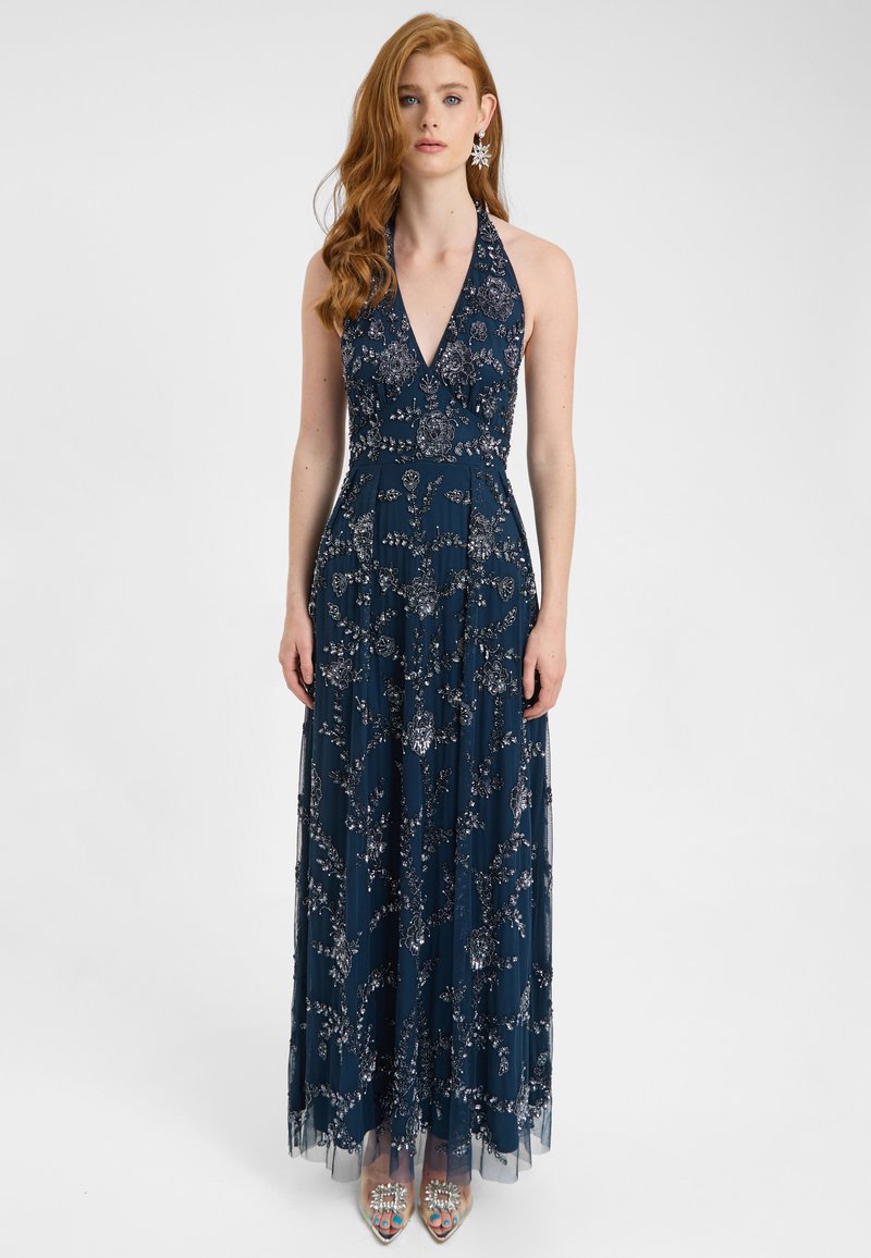 Marineblå halterneck-gown med intrikate perle- og paletmønstre i blomstermønster, lagdelt tylskørt, der når gulvet, parret med klare dekorerede stilethæle.