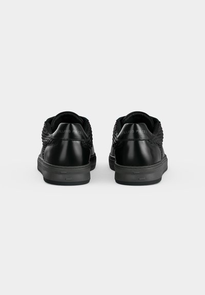 Двойка черни ниски кецове с текстурирани страни и брандиране "Filling Pieces" на петата, гледани отзад на едноцветен фон.
