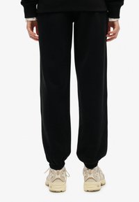 Pantalones deportivos negros con un ajuste relajado, puños elásticos y una textura suave, combinados con zapatillas beige con un diseño de malla.