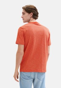 Camiseta de rayas naranjas con cuello redondo y mangas cortas, hecha de un tejido suave y texturizado, vista desde la parte de atrás. Llevada con jeans de color azul claro.