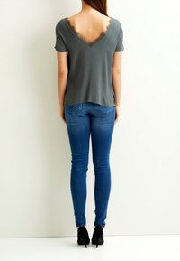 Top gris de manga corta con un amplio escote en V y borde de encaje, combinado con jeans ajustados azules y zapatos de tacón negros.