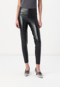 Melnas mākslīgās ādas leggins ar augstu jostasvietu, gludu tekstūru un pieguļošu izskatu, apvienoti ar sudrabainiem papēžiem.