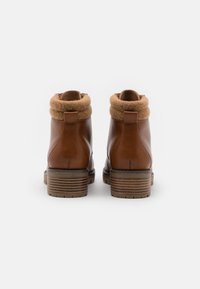 Bottes courtes en cuir marron avec un col en laine beige, dotées d'un talon bloc et d'une semelle texturée. Conçues pour la durabilité et le confort.