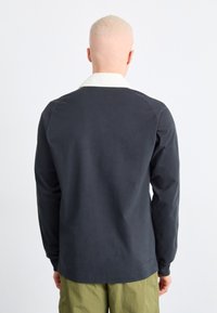 Cămașă cu mâneci lungi din material de culoare bleumarin închis, cu un guler alb în contrast. Prezintă o croială lejeră și un design simplu, cu mâneci lungi.