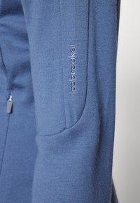 Sweatshirt azul com um tecido suave, design ajustado e bolsos laterais. Logótipo "Icebreaker" bordado na manga direita.