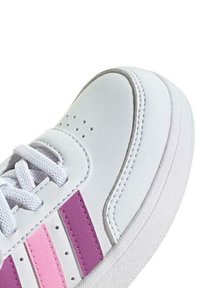 Sneaker bianco con righe rosa e viola, parte superiore in pelle strutturata, suola bianca piatta e punta rotonda. I lacci sono di un grigio chiaro, con perforazioni sui lati.