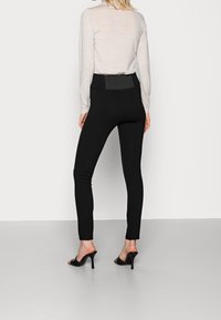 Leggings negros con cintura alta, textura suave y diseño elegante. Combinados con una camiseta de manga larga en gris claro y mules negros con tacón.