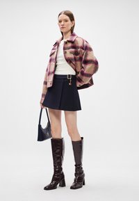 Καρό σακάκι από μίγμα μαλλιού σε ροζ και μπεζ, λευκό τοπ, πλισέ ναυτικό φούστα και μποτάκια μέχρι το γόνατο σε μπορντό με ανάγλυφο σχέδιο κροκολείρας; ναυτική τσάντα.