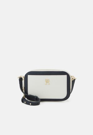 Lille rektangulært sort-hvid crossbody taske med guldfarvet hardware og justerbar rem, med et gyldent logo på frontlommen.