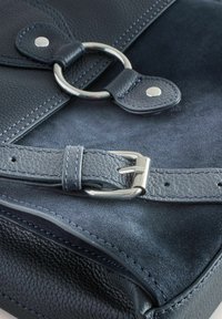 Morska usnjena torba, ki se ponaša z teksturirano površino, srebrno kovinsko opremo, naramnico s sponko in kovinskim obročem kot poudarkom ter kontrastnim šivanjem.