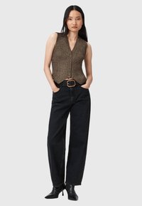Brązowy, dzianinowy top bez rękawów z dekoltem w serek, zestawiony z czarnymi dżinsami o wysokim stanie oraz czarnym paskiem z prostokątną złotą klamrą.
