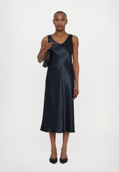 Marine satin uten ermer kjole med V-hals, flytende A-linje silhuett og subtil glans; paret med en svart vevd håndveske og spisse leiligheter.