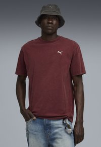Bordeaux bomulds-t-shirt med korte ærmer og rund hals, med et lille hvidt Puma-logo; parret med lyseblå jeans og en grå bøttehat.