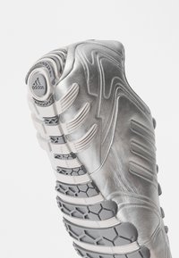 Ασημένιο αθλητικό παπούτσι με κομψό σχεδιασμό, υφασμάτινη συνθετική επένδυση με υφή, λευκές λεπτομέρειες και καπιτονάκ μοντέρνα γκρι σόλα.