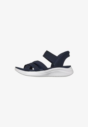 Sandalia azul marino con puntera abierta, tres tiras delanteras y una tira en el tobillo, con suela blanca texturizada y flexible.