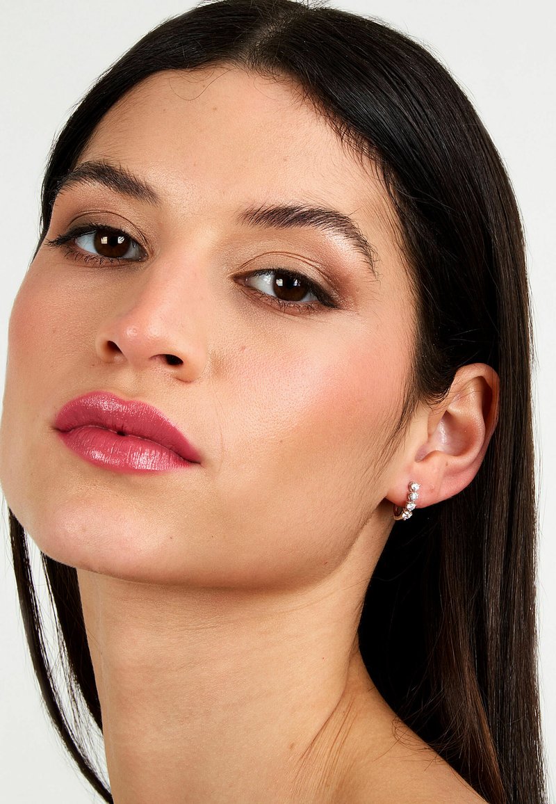 Orecchini a cerchio d'argento con tre strass scintillanti disposti verticalmente, indossati da una modella con pelle liscia e chiara e capelli scuri.