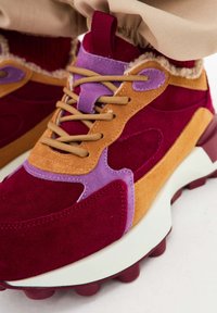 Sneaker multicolore con camoscio borgogna, beige e viola, dotato di una suola bianca spessa e di spiccate texture lungo i lati.