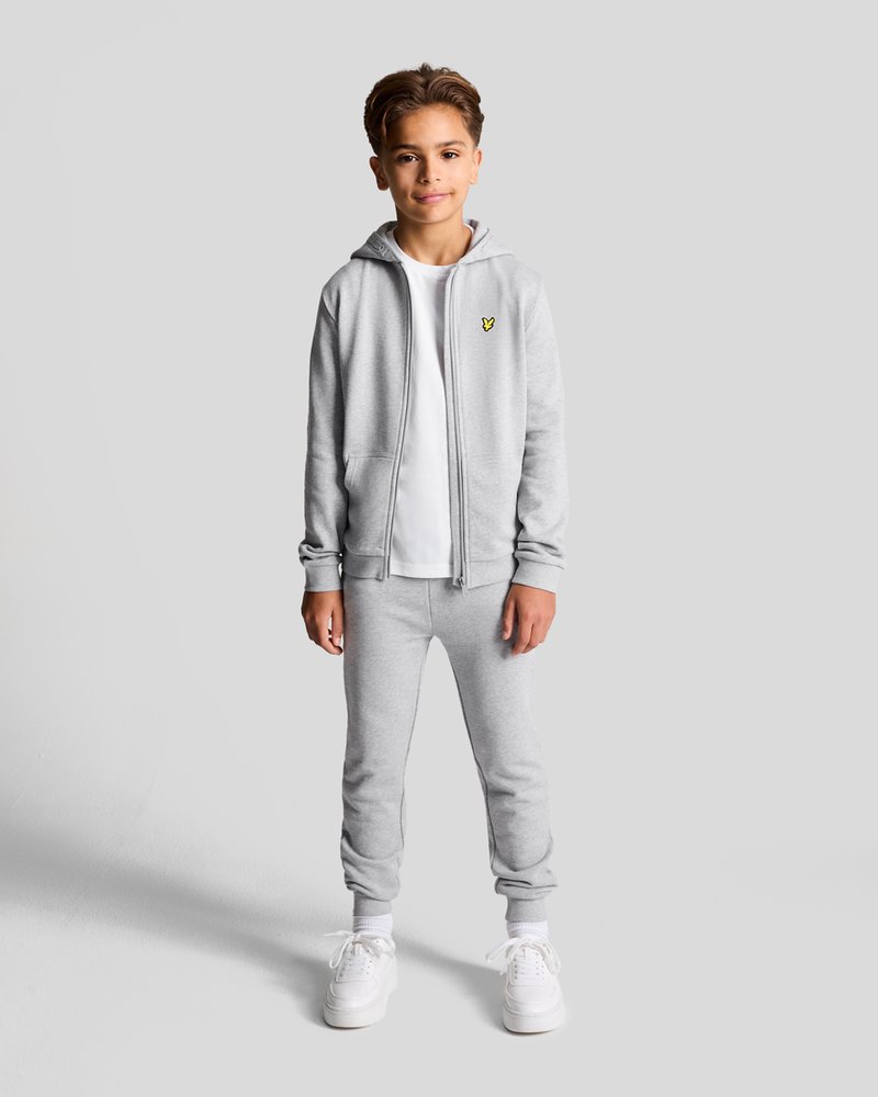 Grå zip-up hettegenser og joggebukse sett, laget av mykt stoff. Har en hvit t-skjorte under og hvite joggesko. Lite gult logo på hettegenseren.