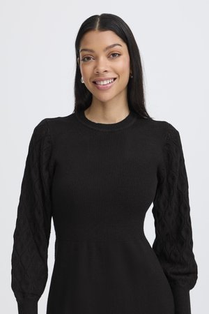 Černé šaty s žebrovaným živůtkem a texturovanými balónovými rukávy s copánkovým vzorem. Hladká látka s jemným leskem a přiléhavý střih.