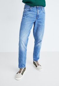 Jeans din denim de culoare albastră deschisă, cu o croială lejeră, având un talie cu nasture, cinci buzunare și decolorări subtile. Puși împreună cu adidași gri și verzi.