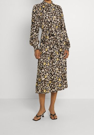 Robe midi à imprimé floral avec manches longues, taille cintrée et col montant, présentant des couleurs blanche, jaune et marron foncé.