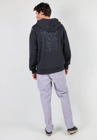 Haut à capuche noir avec un design graphique au dos, associé à un pantalon à rayures claires. Le tissu semble doux ; les poignets et l'ourlet côtelés sont visibles.