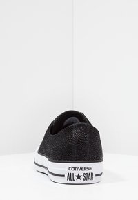 Sneaker nera con texture, dal profilo basso, con suola intermedia in gomma bianca e dettagli a strisce nere. Presenta il marchio "Converse All Star" sul tallone.