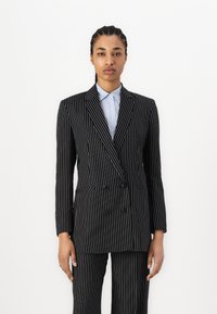 Double-breasted black pinstripe suit with structured shoulders, contrasting white stripes, and a collared blue striped shirt underneath.