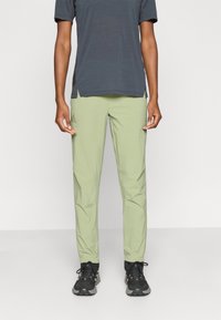 Φωτεινό πράσινο, στενά εφαρμοστά παντελόνια κατασκευασμένα από λείο, ελαφρύ ύφασμα. Διαθέτουν πλαϊνές τσέπες και ελαφρώς στενό πόδι. Συνδυασμένα με σκούρο γκρι τοπ.