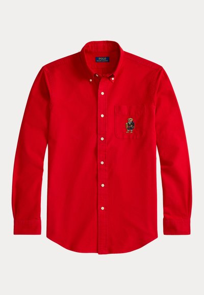 Κόκκινο βαμβακερό πουκάμισο με κουμπιά, διαθέτει τσέπη με κεντημένο σχέδιο αρκούδας. Έχει μακριά μανίκια και κλασικό γιακά.