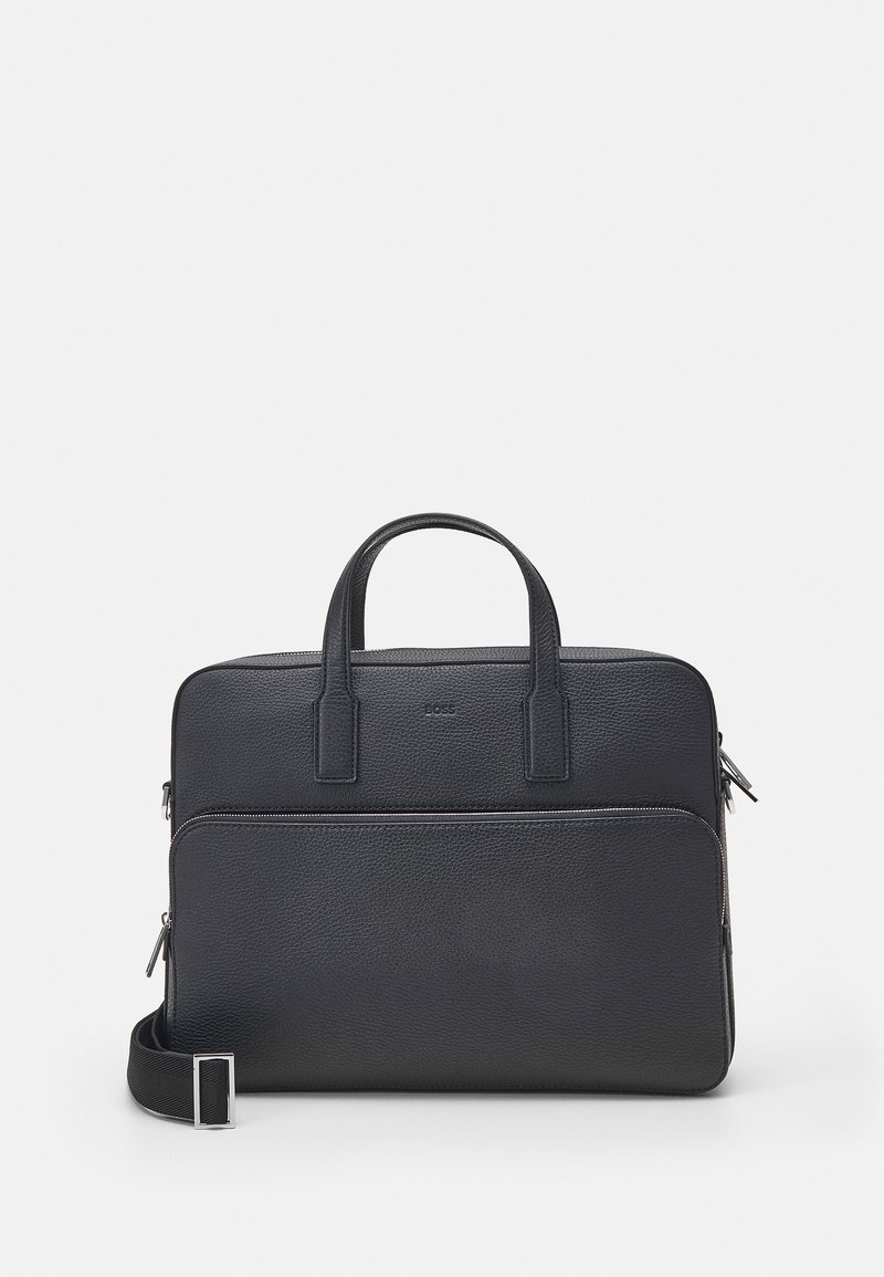 Serviette en cuir noir texturé avec poignées supérieures, poche avant zippée et bandoulière réglable sur fond uni.
