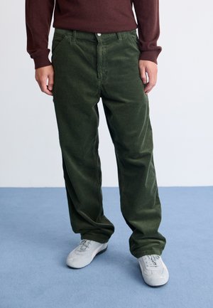 Pantalones de pana verde oscuro con un diseño recto, que cuentan con un cierre frontal de botones y bolsillos laterales, combinados con zapatillas deportivas grises.