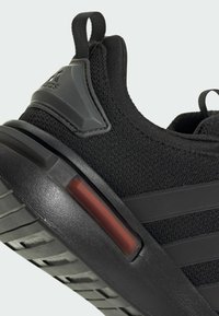 Gros plan sur le talon d'une chaussure de sport noire avec un tissu texturé, une semelle en caoutchouc, une languette de traction et un insert rembourré rouge dans la semelle intermédiaire.