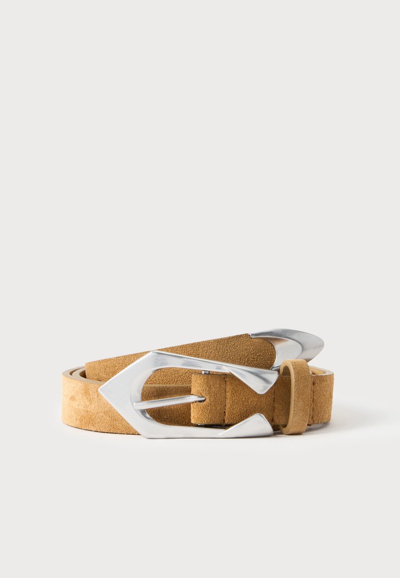 Ceinture en daim marron clair avec une grande boucle en métal argenté pointue, enroulée sur un fond blanc uni.