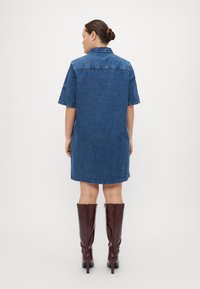 Jeansjurk met korte mouwen en een kraag, met een relaxte pasvorm, rafelrand en een rugnaad detail. Gepaard met hoogglanzende burgunderbine laarzen tot de knie.