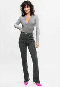 Grijze geribbelde longsleeve bodysuit met een diepe V-hals, gecombineerd met hoge, donkere grijze flared jeans en felroze pumps met puntige neuzen.