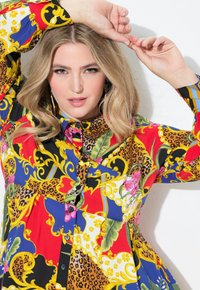 Camisa de botones colorida que presenta una mezcla de patrones florales, de animales y barrocos en rojo, azul, amarillo y negro, con un cuello tipo polo.