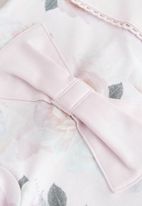 Fiocco di tessuto rosa tenue su tessuto chiaro con motivo floreale e sottili foglie verdi, con dettaglio di bordatura cucita.