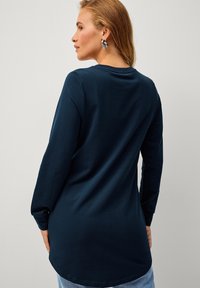 Mørkeblå langærmet skjorte med rund kant, lavet af blødt stof. Har en rund halsudskæring og bæres med lyseblå jeans.