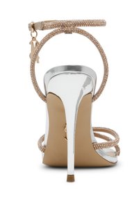 Heldere gouden strappy high-heeled sandaal met een glanzende zilveren hak, voorzien van een slanke enkelband en een klein logo charm, versierd met rhinestones.