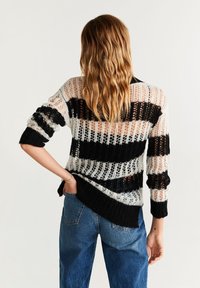 Maglione lavorato a maglia con motivo a righe in nero e bianco, caratterizzato da una texture morbida e ariosa e maniche a tre quarti. Indossato con jeans a vita alta.