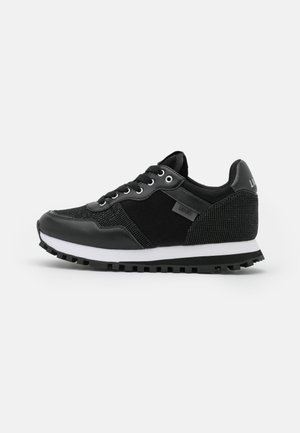 Zapatilla negra con suela blanca, tejido texturizado y paneles de cuero, con cordones delanteros y suela exterior resistente y con dibujo, mostrada de perfil.