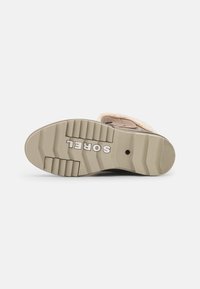 Winterbootzool met diepe profiel en "SOREL" branding, beige rubberen tussenzool, en een glimp van de tan bovenkant met bontvoering.