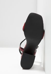Sandale à lanières rouge et noire avec un motif texturé en peau de serpent, bout ouvert et semelle noire lisse et plate.