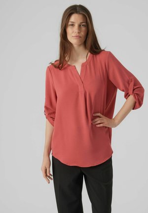 Blusa de color coral con cuello mandarina, mangas 3/4 y detalles de tiras enrollables. Fabricada en un tejido suave con un ajuste ligeramente drapeado.