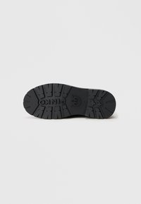 Juodas gumos batų padas su tekstūruotu protektoriumi, įskaitant logotipo detalę ir pakeltas zonas sukibimui.