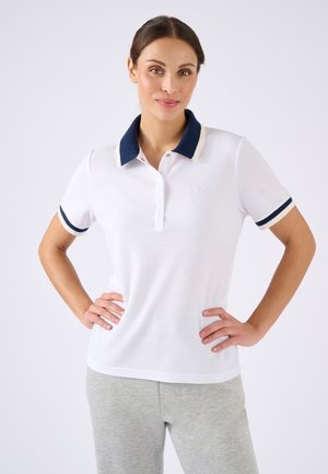 Chemise polo blanche avec col et accents de manches navy, dotée d'une patte de boutonnage et d'un petit logo sur la poitrine gauche. Texture lisse.