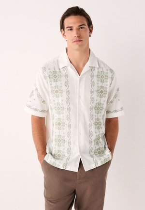 Short-sleeve, button-up shirt in white fabric, featuring green embroidery with floral and geometric patterns along the front and sleeves.