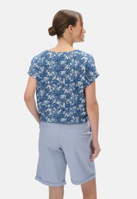 Niebieska i biała bluzka z krótkim rękawem w wzory, zestawiona z jasnoniebieskimi szortami z podwiniętymi nogawkami, w luźnym kroju i o miękkiej strukturze materiału.